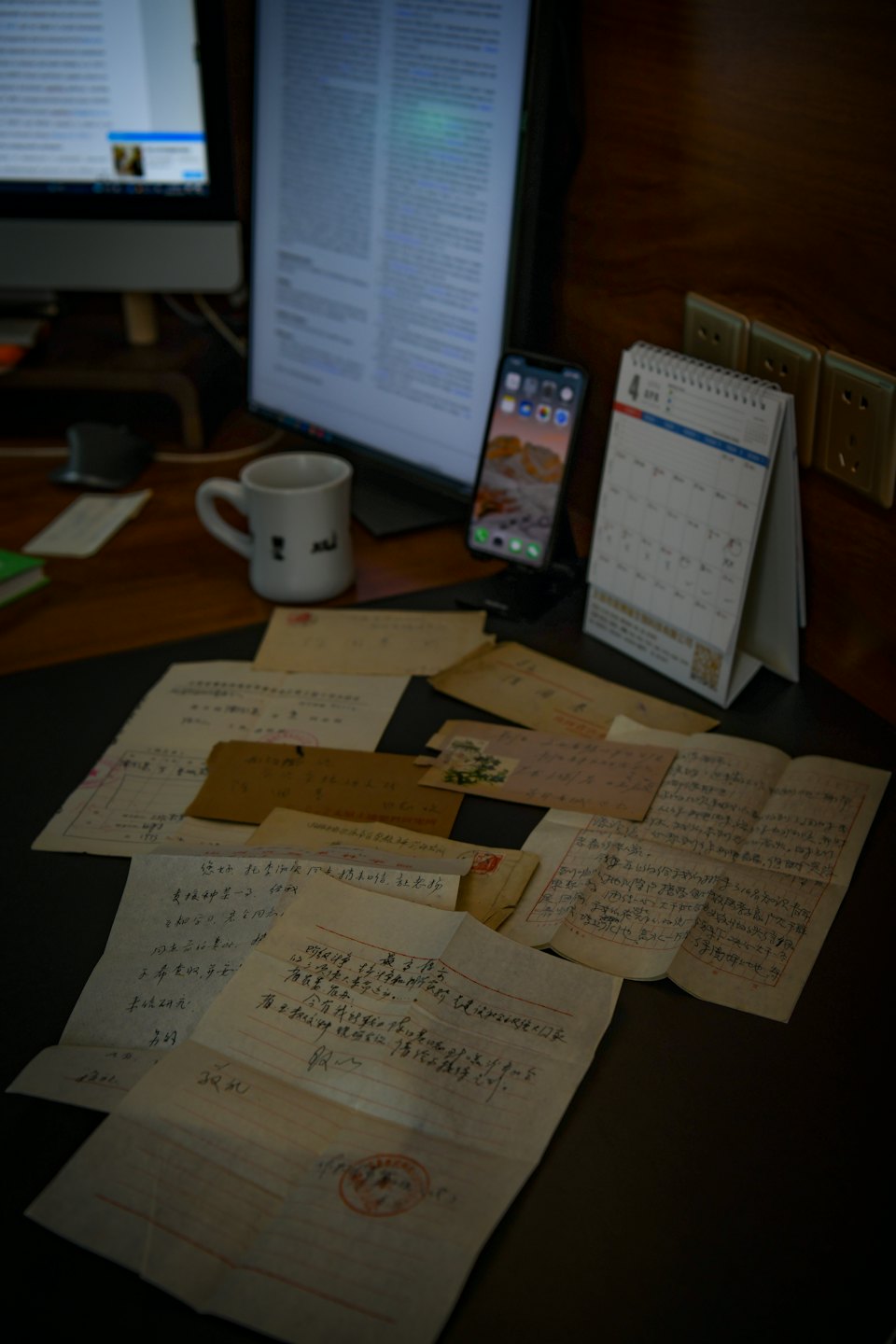 Ručně psané historické dokumenty leží na stole s moderní technologií.