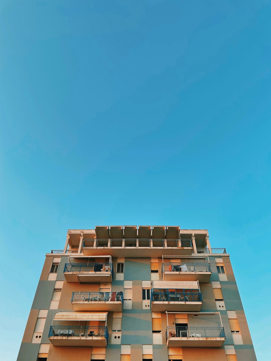 Moderní bytový dům s balkony pod jasně modrou oblohou.